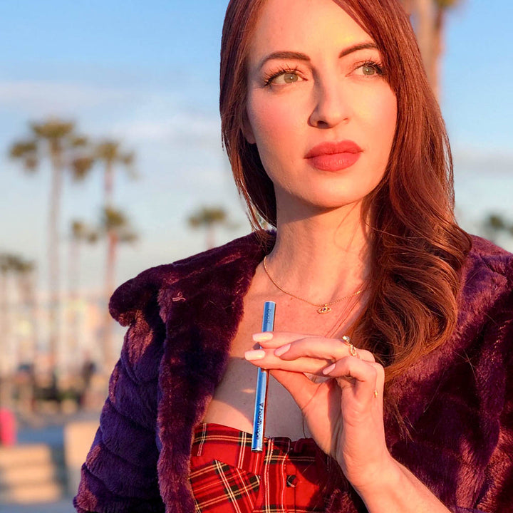 Woman holding HealthVape Boost Berry Mint disposable vape pen with palm trees in background