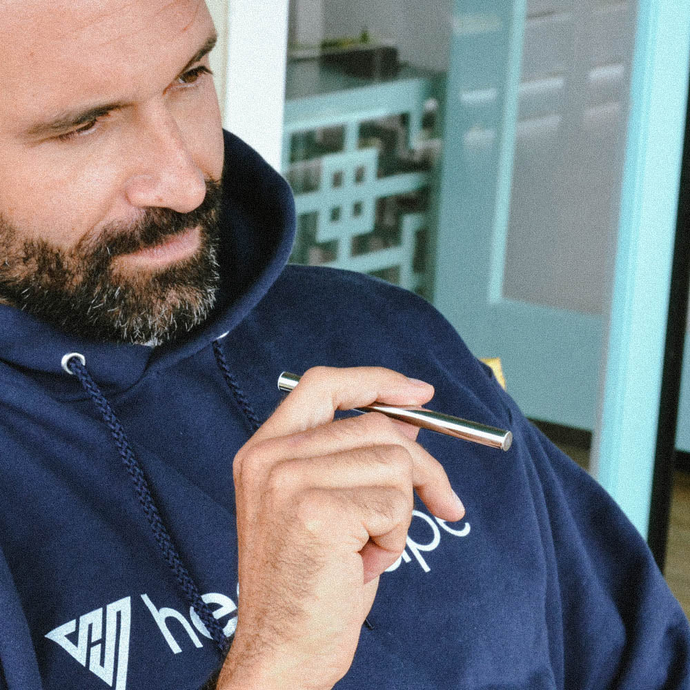 Man in navy hoodie holding silver HealthVape Boost vape pen indoors