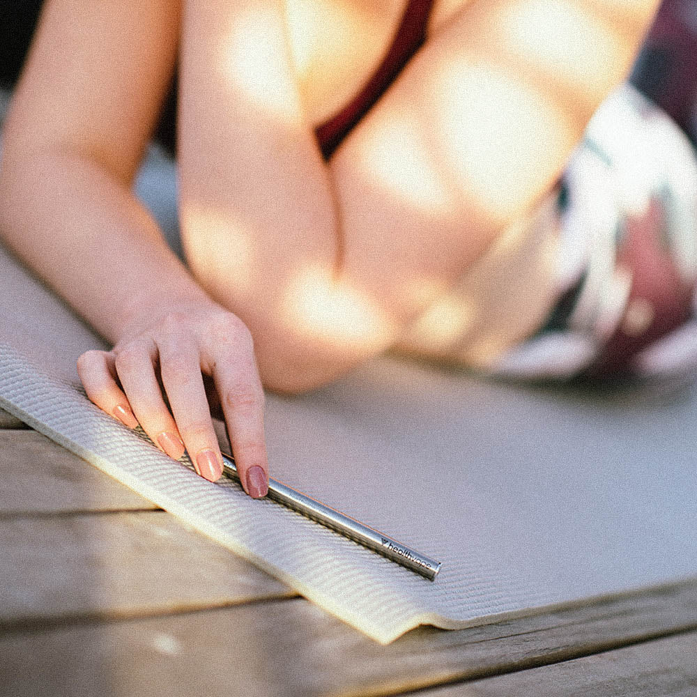 Person lying on a yoga mat outdoors, holding a HealthVape BOOST Vitamin B12 disposable inhaler in hand.