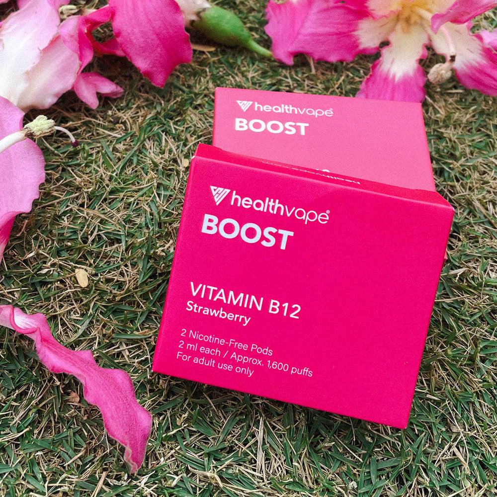Two HealthVape BOOST Strawberry pod boxes on grass with pink flower petals
