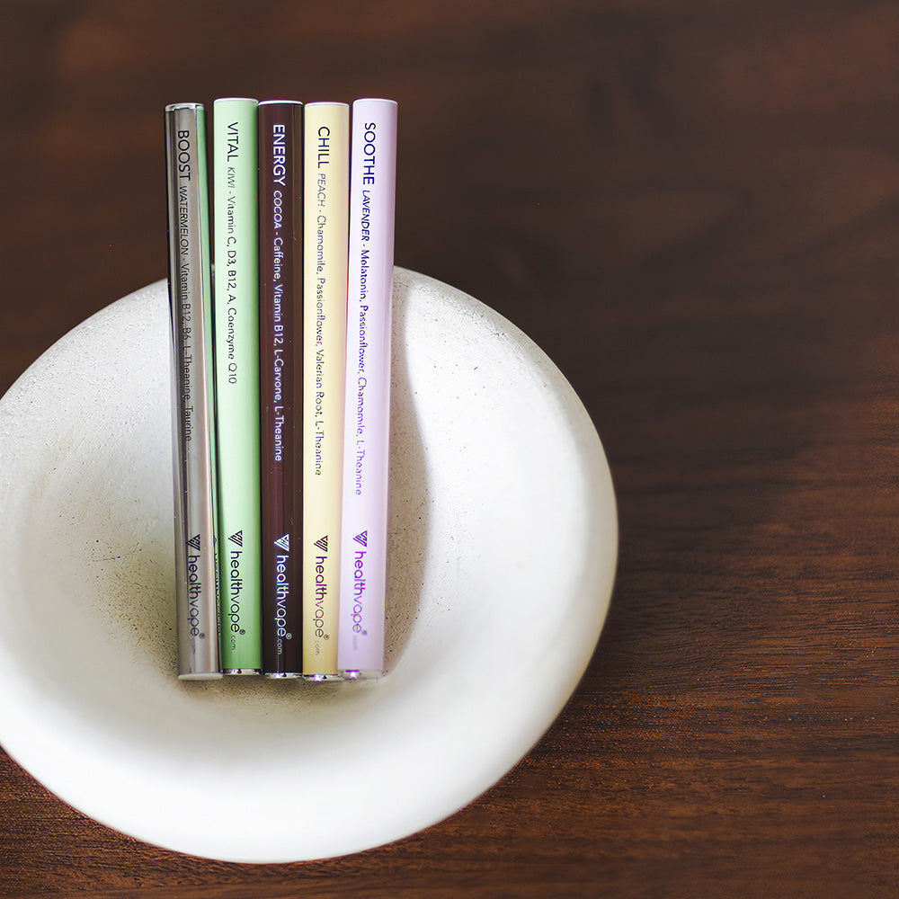 Five HealthVape pens in assorted flavors displayed in a white bowl on wooden surface