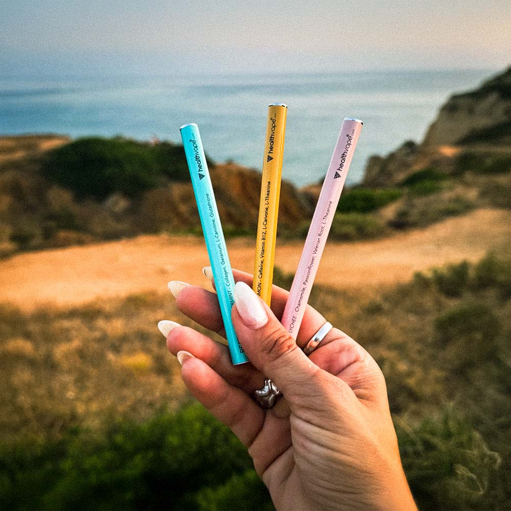 Hand holding three colorful HealthVape pens — Restore, Energy, and Soothe — with an ocean cliff background.