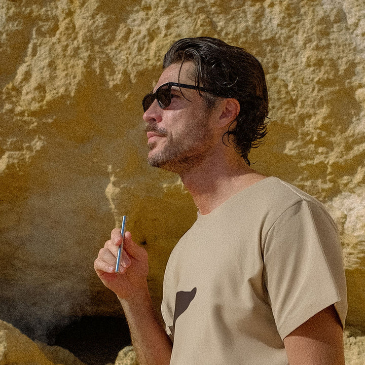 Man wearing sunglasses and beige shirt holding a HealthVape pen against yellow wall