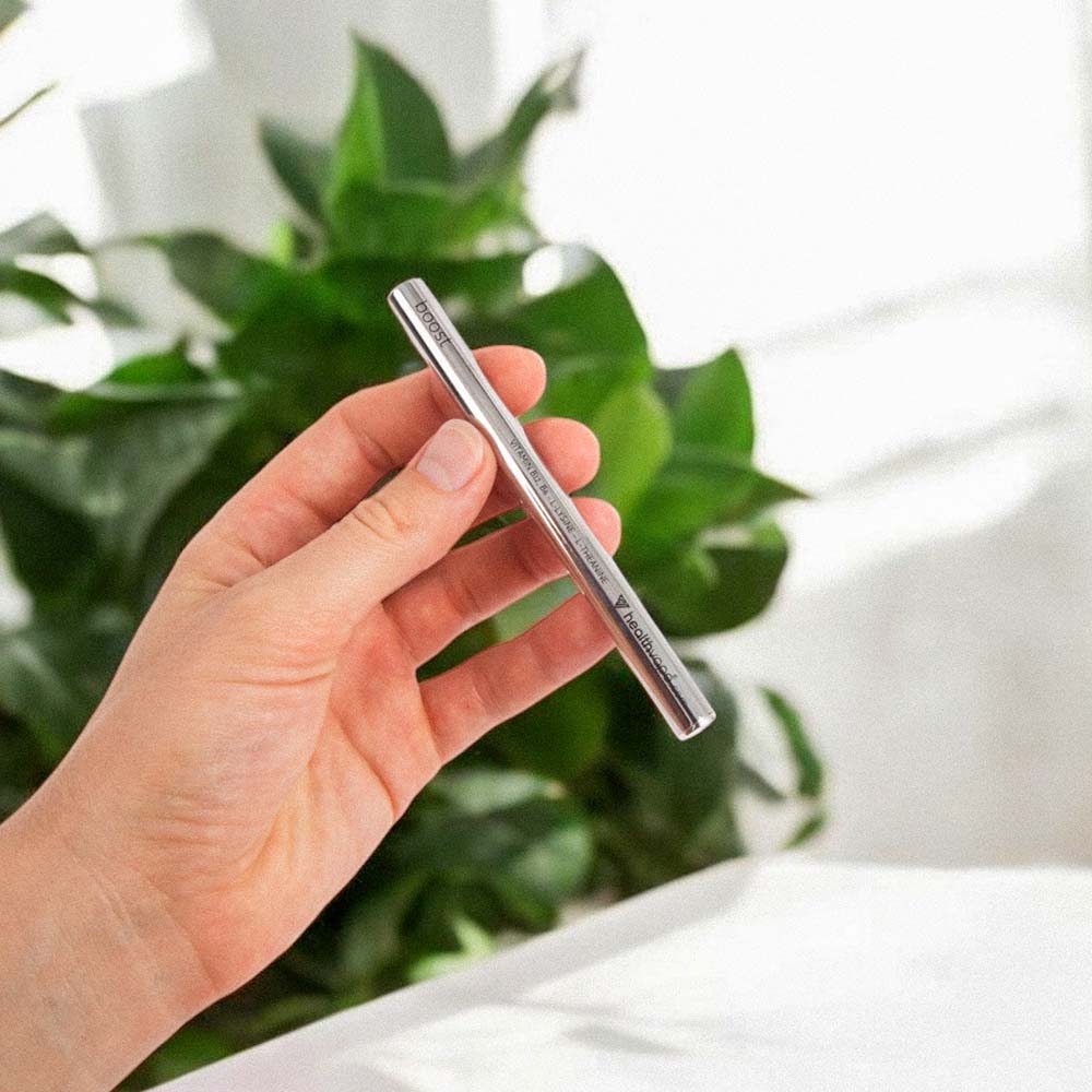 Hand holding silver HealthVape Boost vape pen with green plants in background