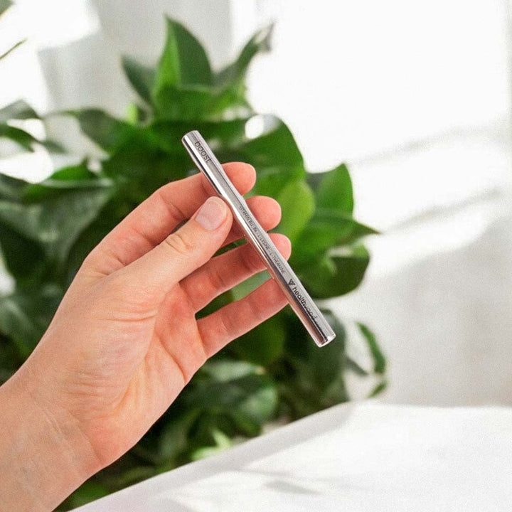 Hand holding silver HealthVape Boost vape pen with green plants in background