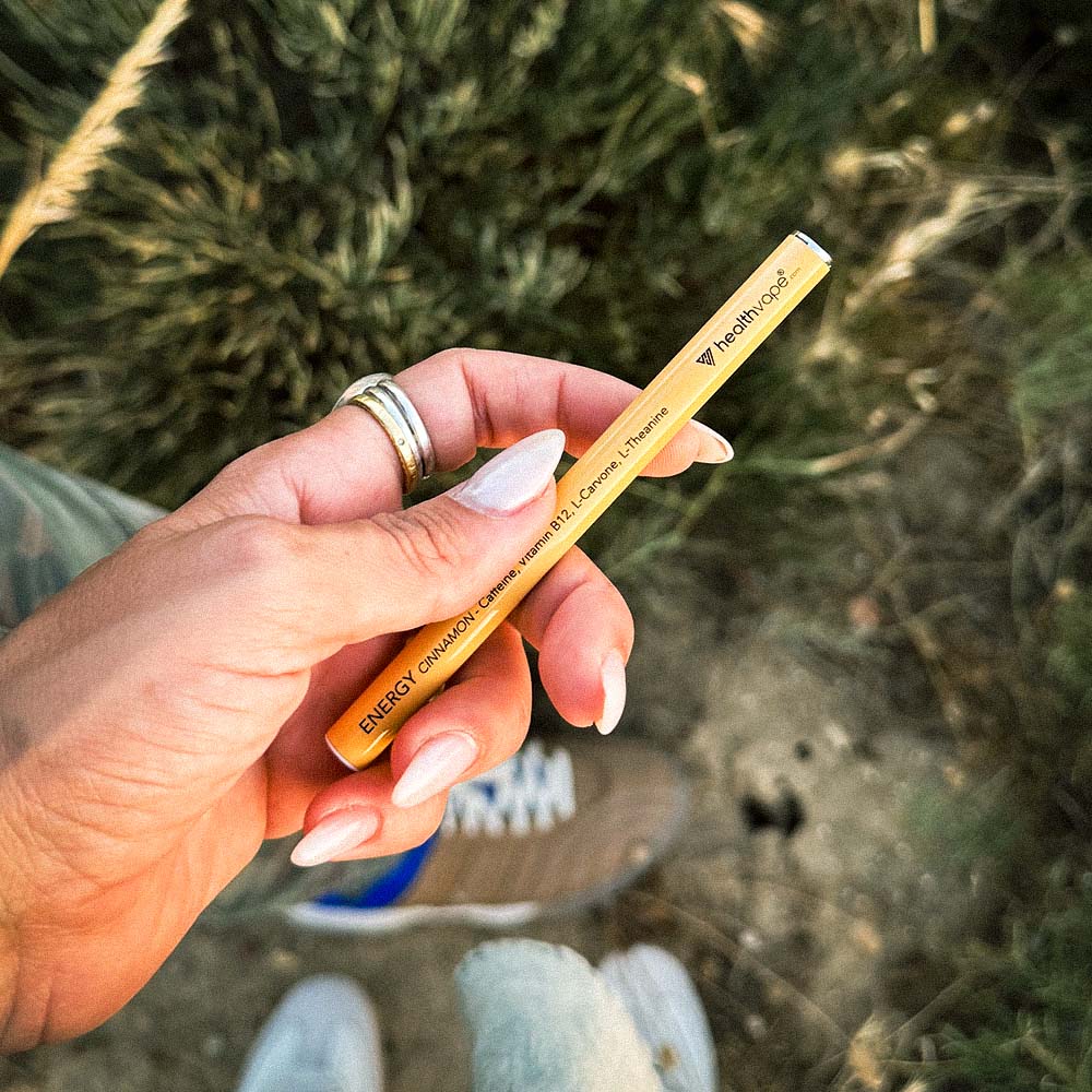 Hand holding a yellow HealthVape Energy vape pen infused with caffeine, vitamin B12, L-Carnitine, and L-Theanine.