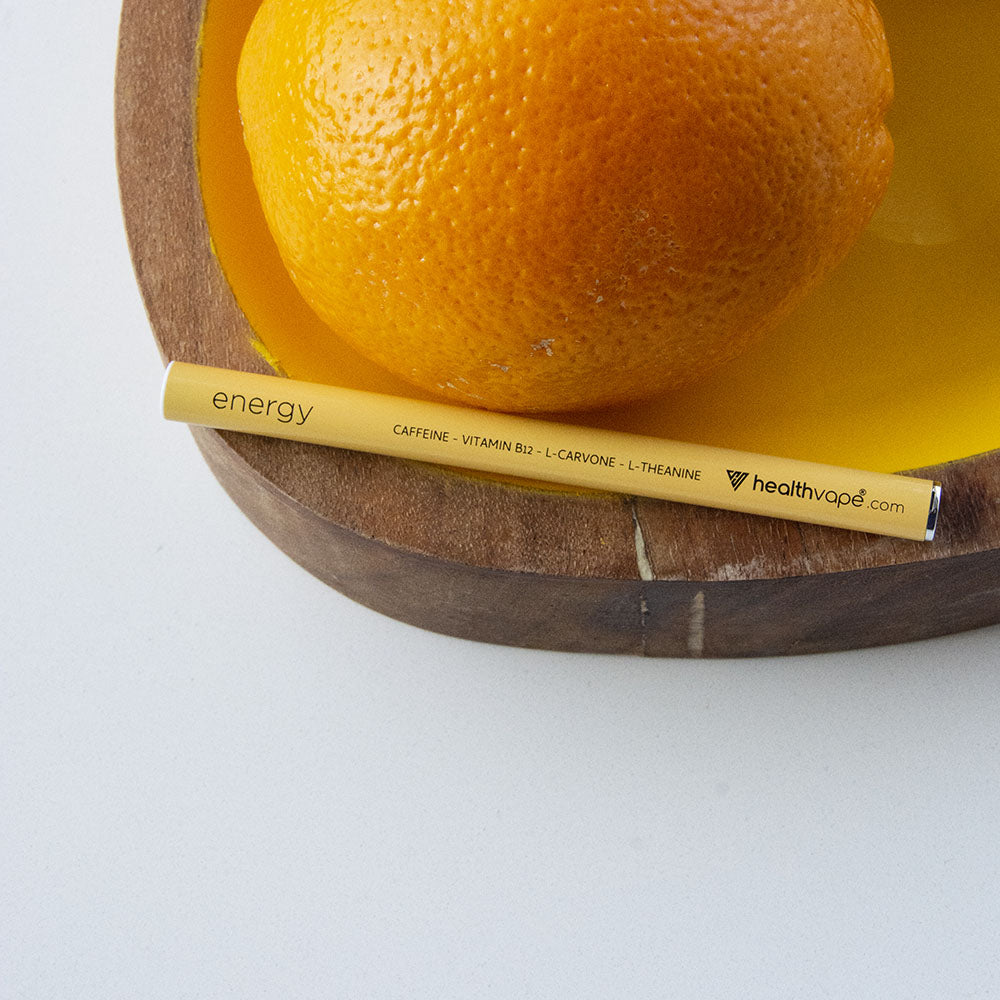 HealthVape ENERGY Citrus disposable inhaler placed on a wooden tray beside a fresh orange.