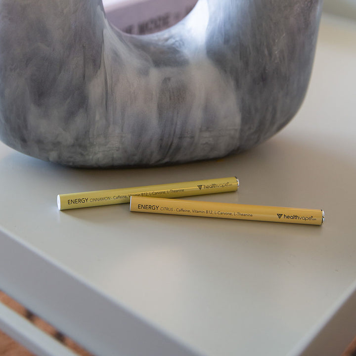 Two HealthVape ENERGY disposable inhalers, Citrus and Cinnamon flavors, placed on a white surface near a decorative vase.