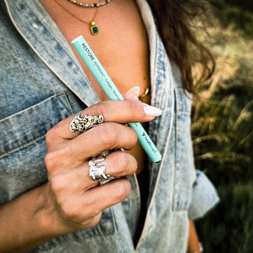 Woman holding a turquoise HealthVape Restore vape pen with peppermint collagen formula.