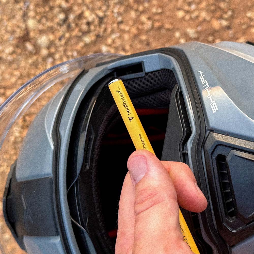 Hand holding a yellow HealthVape Vital vitamin vape pen near a motorcycle helmet.