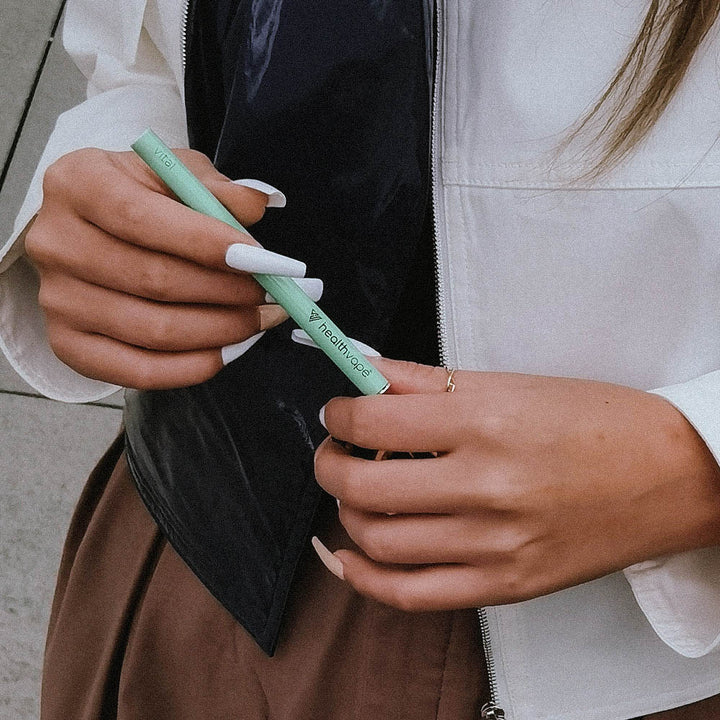 Person holding a green HealthVape VITAL disposable inhaler, designed with a wellness vitamin blend.