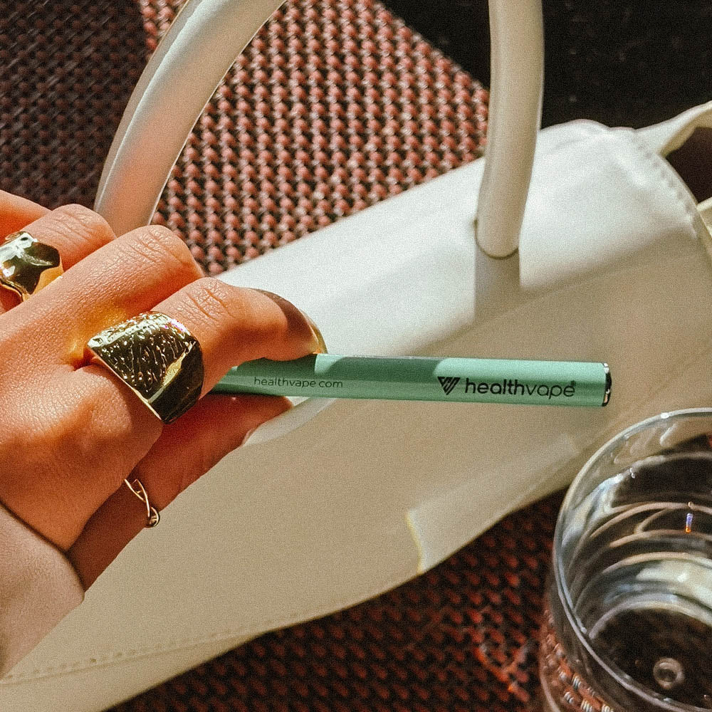 Hand holding HealthVape Vital Vitamin C Minty Lime disposable vape pen with bag in background