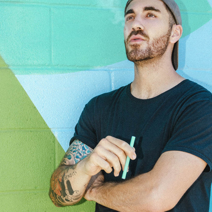 Man holding HealthVape Vital Vitamin C Minty Lime disposable vape pen against colorful wall