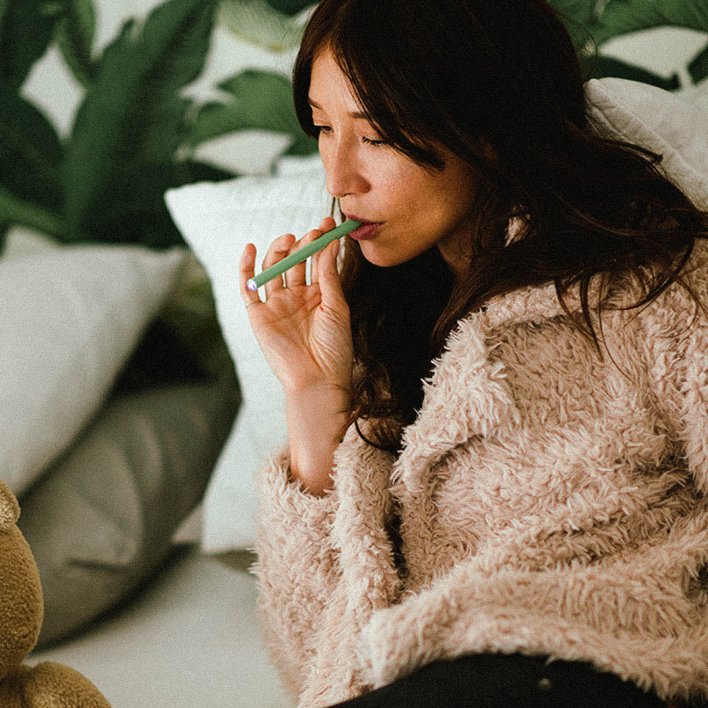 Woman in cozy setting using green HealthVape Vital Vitamin C Kiwi pen
